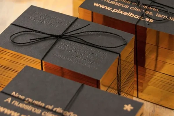 Luxury business cards with gold edges and embossed text, tied with black string.