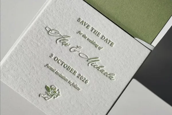 Wedding invitation card with embossed text and green envelope.